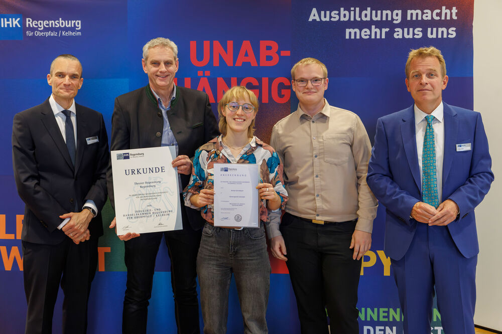 Annika Schmidbauer (Mitte) zwischen dem stellvertretenden Werkstattleiter Thomas Schroll (links) und Tobias Schnepf, Leiter Malersaal (rechts) bei der Urkundenverleihung durch die IHK, flankiert von IHK-Präsident Christian Volkmer (l.) und dem stellv. IHK-Hauptgeschäftsführer Peter Weber (r.)